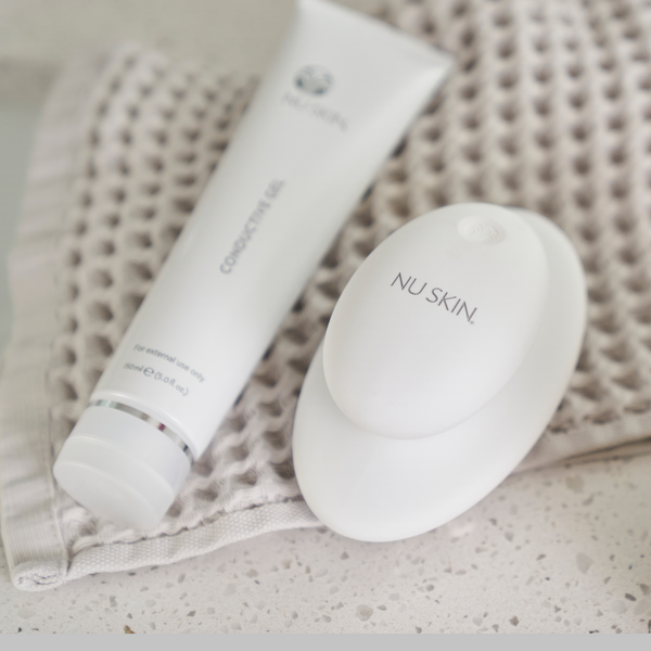 A tube of Nu Skin Conductive Gel and the RenuSpa iO device lying on a hand towel. 