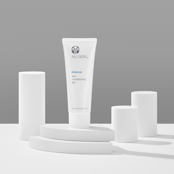 Bottle of Nu Skin Enhancer skin conditioning gel surrounded by white, abstract geometric objects.